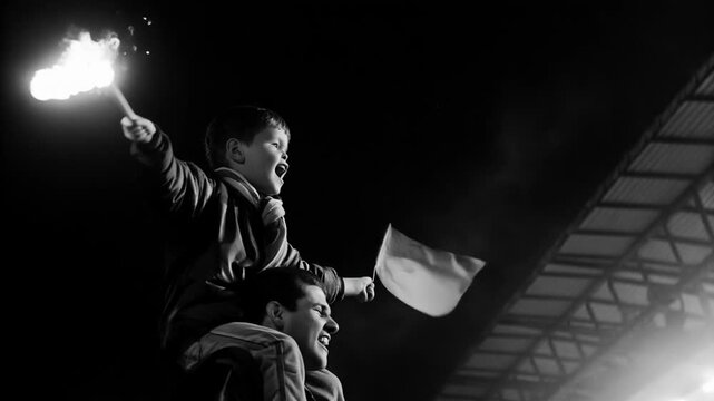 Football fans cheering loudly in night stadium concept. A child joyfully waving a flag on an adult's shoulders amidst a lively crowd.