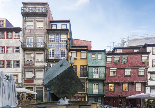View of a modern cube fountain amidst the colorful, tiled facades of old buildings under a soft sky, Porto, Porto District, Portugal.