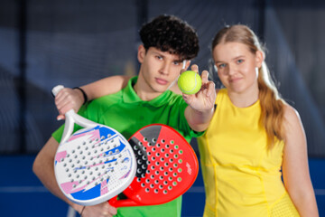 Indoor padel doubles players showing ball and rackets before match