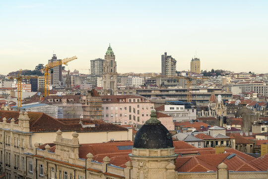 View of terracotta rooftops blending into the urban skyline, punctuated by historical towers and modern construction cranes, Porto, Porto District, Portugal.