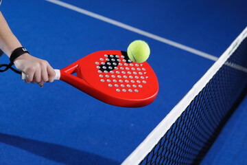 Padel racket volley closeup with ball over net on indoor blue court
