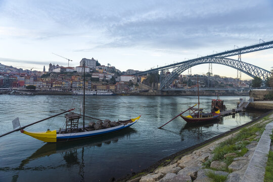 View of traditional boats rest on the Douro River's edge beneath the Dom Lu&Atilde;&shy;s I Bridge, as the city of Porto rises in the background, Porto, Porto District, Portugal.