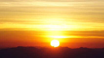 Warm sunrise above mountain range with glowing sky
