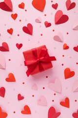 Valentine's Day vertical card with paper hearts and red gift box on pink background top view.