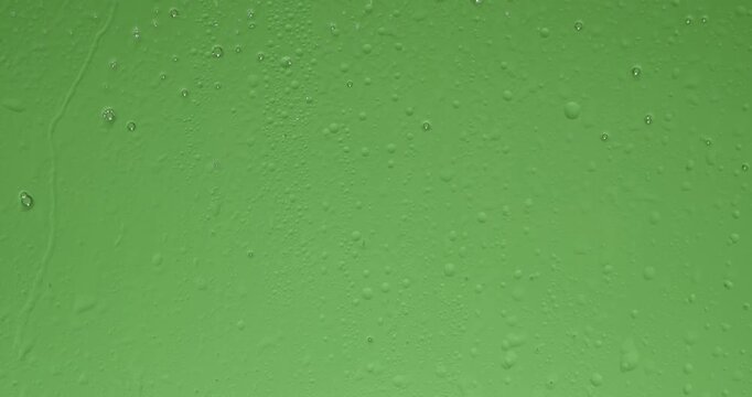 A close up of wet glass with dripping foam and small bubbles against a green background chroma key. Ideal for visual effects and background replacement. Slow motion.