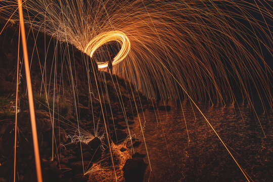 View of fiery sparks cascade down a rocky cliff in a dazzling display of light painting against the dark night sky, Isle of Skye, United Kingdom.
