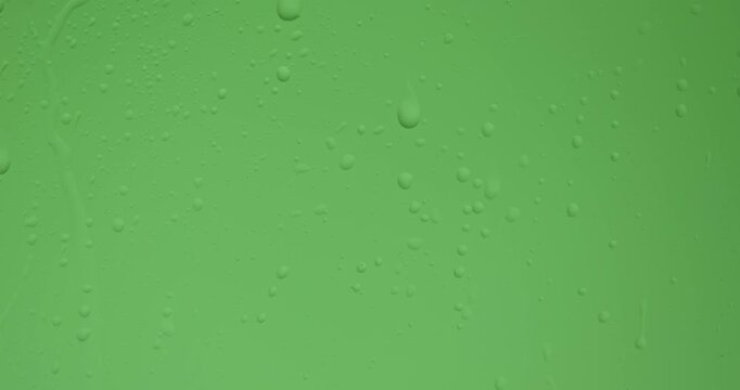 Close up of wet glass with dripping water drops and streaks of rain, on a bright green chroma key background, perfect for visual effects and background replacement. Slow motion.