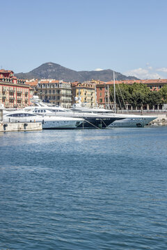 View of turquoise waters gently lapping against the harbor where gleaming white yachts nestle beneath colorful buildings, all under a clear sky, Nice, France.