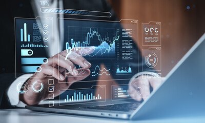 Digital interface showing graphs and stock charts on laptop with businessman analyzing forex market data using futuristic hologram screen technology concept.