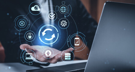 Businessman presenting digital data synchronization concept with glowing icons on futuristic interface against dark blurred background.