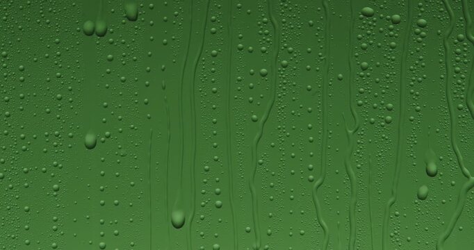 Close up of wet glass with dripping water drops and streaks of rain, on a bright green chroma key background, perfect for visual effects and background replacement. Slow motion.