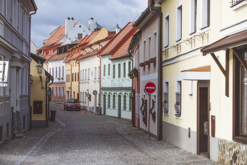 View of pastel buildings lining a cobblestone street under a cloudy sky, the red tile roofs contrasting with the muted facades, Cesky Krumlov, South Bohemian Region, Czechia.