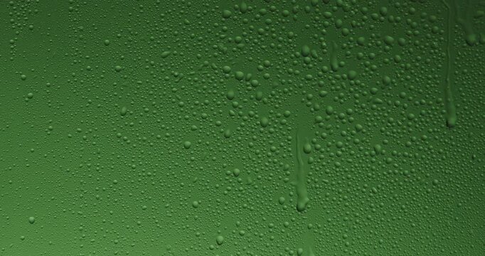 Close up of wet glass with dripping water drops and streaks of rain, on a bright green chroma key background, perfect for visual effects and background replacement. Slow motion.