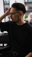 Attractive young brunette man sitting in a barber chair adjusting his new haircut
