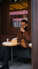 Young man in a jacket sits on an open cafe terrace on an autumn day drinking matcha latte