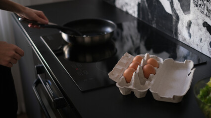 Young slim brunette man cooking scrambled eggs for breakfast in his modern stylish kitchen early in the morning