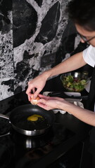 Young slim brunette man cooking scrambled eggs for breakfast in his modern stylish kitchen early in the morning