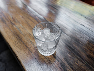 minimal scene of glass with ice on wooden floor