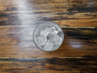 minimal scene of glass with ice on wooden floor