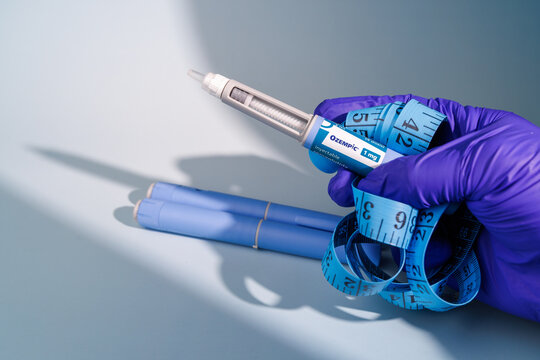 Hand holding Ozempic 1 mg semaglutide GLP-1 pens with a blue measuring tape on a blue gradient background for medical weight loss ads.  In Barcelona - Spain, January 10, 2026.