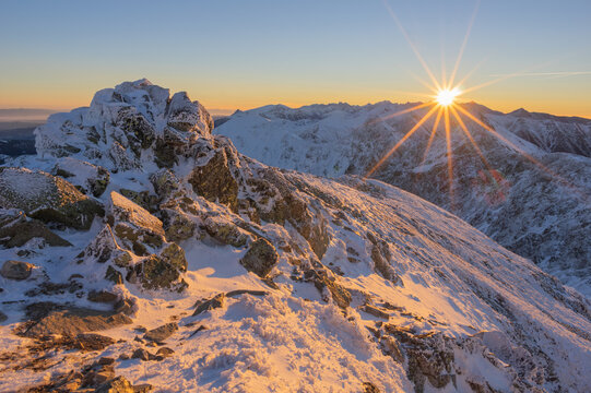 View of a snow-dusted mountain peak kissed by the golden light of the rising sun, creating a stunning contrast of warm and cold hues, Zapadne Tatry, Zilina Region, Slovakia.