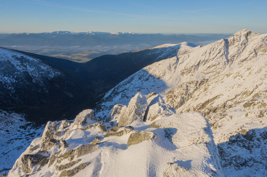 View of snow-dusted peaks and valleys under a crisp blue sky, with rocky outcrops creating a striking foreground in Tri Kopy, Zilina Region, Slovakia.