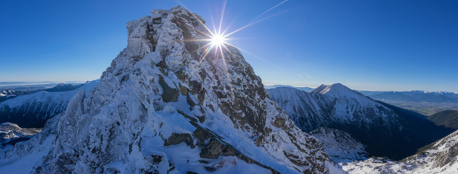 View of a snow-dusted mountain peak piercing the clear blue sky, with sunlight creating a radiant starburst effect, Tri Kopy, Zilina Region, Slovakia.