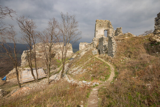 View of weathered stone walls of G&Atilde;&frac12;me&Aring;&iexcl; Castle ruins stand against a moody sky, a path cutting through the wild grass, Jelenec, Nitra Region, Slovakia.