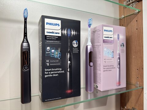 Philips Sonicare toothbrushes in two colors: black and pink. The toothbrushes are on a glass shelf next to the original box. Bathroom interior, theme of daily hygiene and household technology.