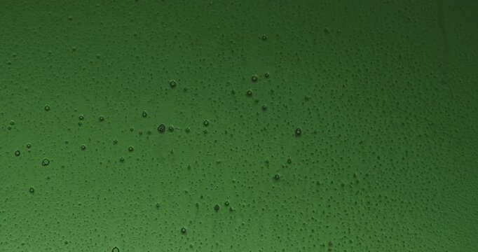 The silhouette of a hand spraying cleaning fluid from a spray bottle onto glass and wiping condensation from a green glass surface. Water droplets and moisture remain on the fogged window. Slow motion