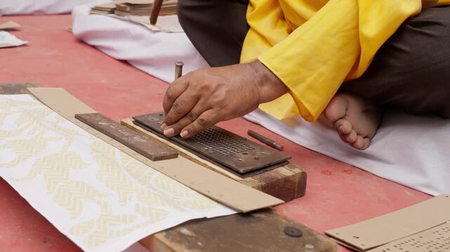 Close view of Indian artisan punching Jacquard cards by hand using hammer and tool to create weaving patterns for traditional silk sarees like Banarasi and Kanchipuram.