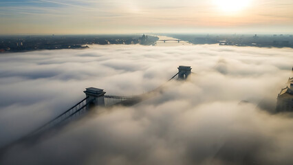 Obraz premium budapest foggy morning aerial view of szechenyi chain bridge emerging from dense fog at sunrise showcasing the danube river cityscape for european travel