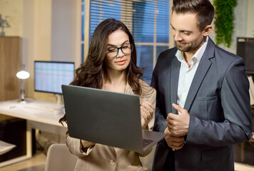 Coworkers colleagues in office discuss business on laptop. Focused woman leads discussion while man listens. They are planning a proposal in an office. Concept shows teamwork and collaboration.