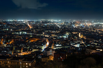 A stunning night cityscape of Naples viewed from a height, showing thousands of city lights, dense urban architecture, and the dark horizon. Naples, Italy