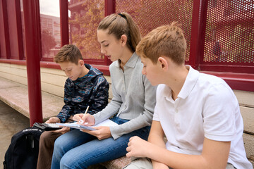 Three siblings studying homework together outdoors