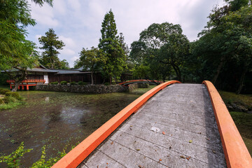 Red curve arching bridge over pond in garden of Usa shrine, Oita
