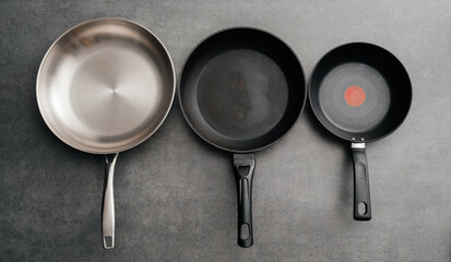 Trio of cookware with matching handles displayed together, Series of three stainless steel frying pans with distinct nonstick and speckled finishes arranged side by side