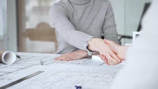 Handshaking between two architects finalizing a construction project deal, business partners agreeing on engineering blueprints and architectural models in an office, close up
