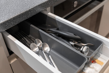 Open kitchen drawer neatly organized with various kitchen utensils and cutlery in a modern grey storage tray, representing home organization and efficient cooking space
