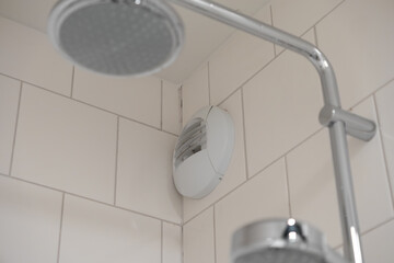 White bathroom extractor fan precisely installed in a clean tiled shower corner, ensuring efficient ventilation and fresh air circulation for a hygienic space