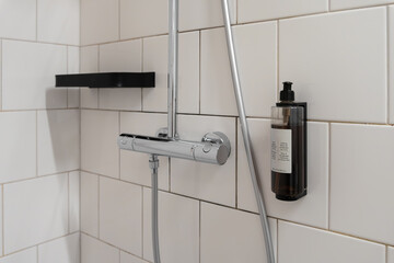Modern bathroom shower setup featuring a chrome mixer faucet, wall-mounted soap dispenser, and sleek black shelf, offering essential hygiene for guests