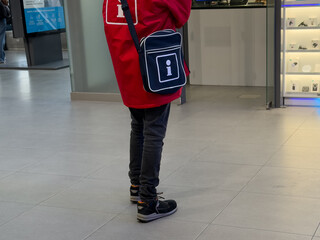 Professional person wearing a red jacket with a clear i information symbol, offering guidance and customer assistance in a busy public service area