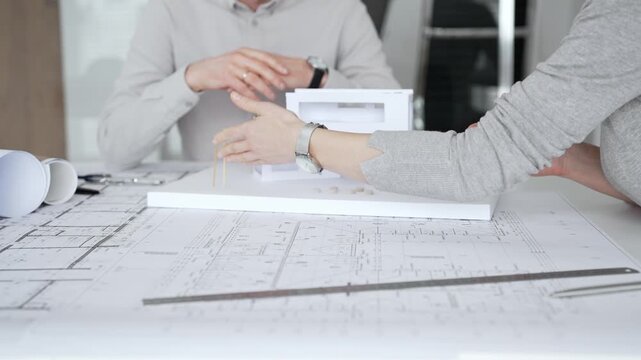 Handshaking between two architects finalizing a construction project deal, business partners agreeing on engineering blueprints and architectural models in an office, close up