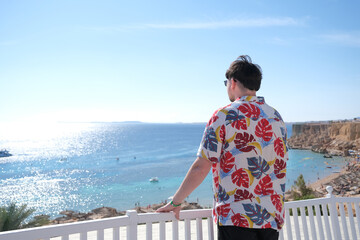 Obraz premium young man in Hawaiian shirt standing on terrace overlooking red sea, Egypt