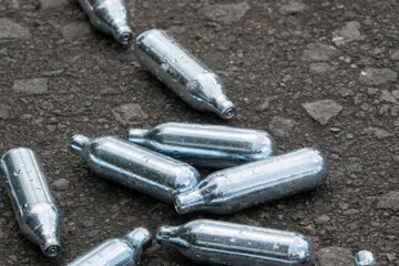 Discarded nitrous oxide gas cartridges on asphalt ground, pollution and waste concept