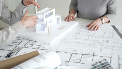 Architects collaborating, examining building blueprints with rulers and pens, developing innovative architectural designs and construction plans around a model house, close up - Powered by Adobe