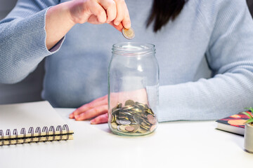 Close up of coins being added to transparent money jar. Represents traditional saving methods and conscious money management for future security