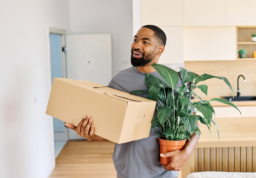 Young black man guy moving into a new modern house, carrying boxes and arriving home. Happy, excited and smiling male student walking, entering and relocating after buying or renting, an apartment