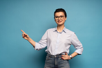 Happy business woman wearing blue shirt looking at camera pointing finger, presenting advertising...