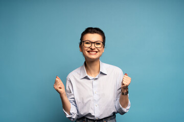 Extremely happy woman standing with raised clenched fists, winning lottery, celebrating her success isolated on blue